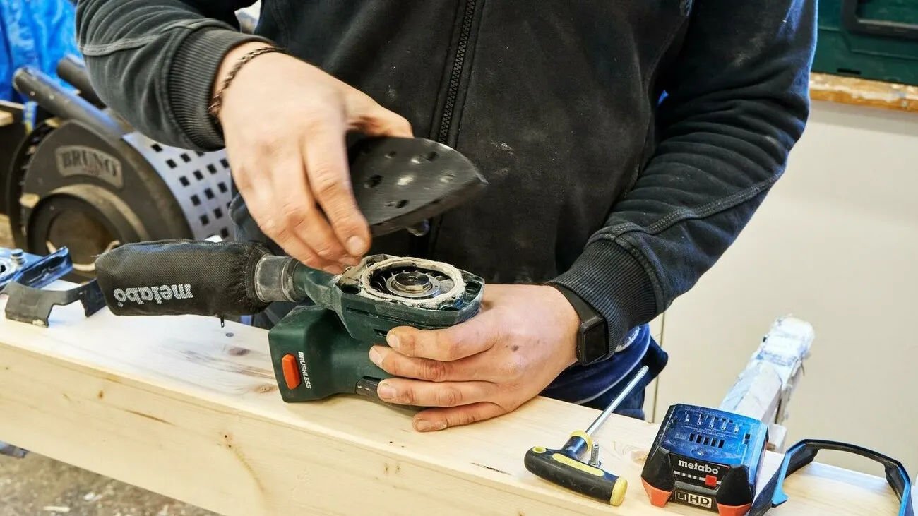 Handwerker hält den Akku-Multischleifer und setzt die Schleifplatte drauf.